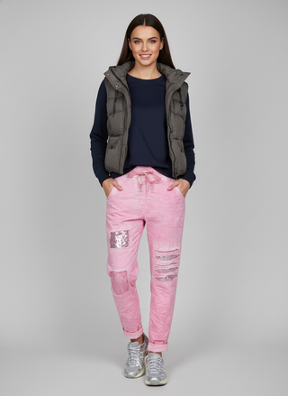 Woman wearing pink jeans with patches and a dark jacket on a gray background