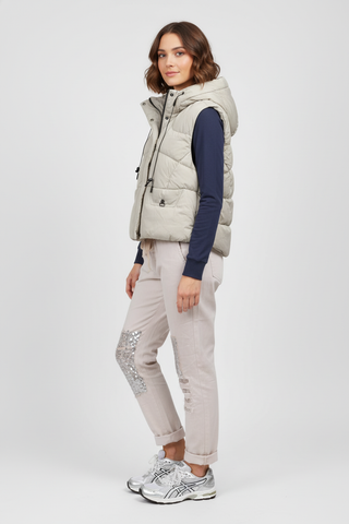 Woman wearing a light gray puffer vest over a dark blue long-sleeve shirt and beige pants on a white background