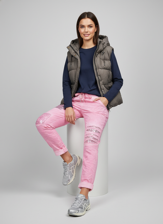 Woman wearing a gray puffer vest, navy long-sleeve top, pink pants, and silver sneakers on a gray background