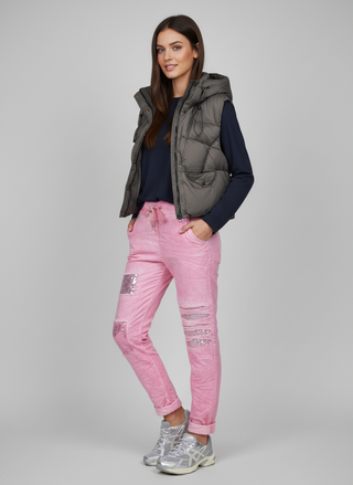 Woman wearing a gray puffer vest, navy shirt, pink jeans, and silver sneakers on a gray background