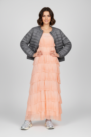 Woman wearing a peach dress with a gray puffer jacket on a white background