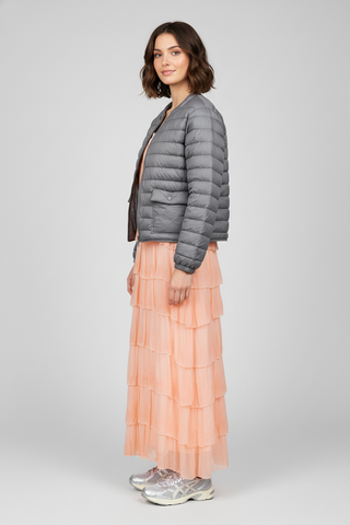 Woman wearing a gray puffer jacket and peach layered skirt on a white background