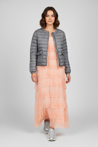 Woman wearing a gray puffer jacket over a peach dress on a white background